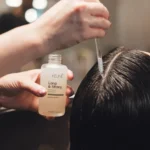 Een kapper die een serum aanbrengt op de hoofdhuid van een klant