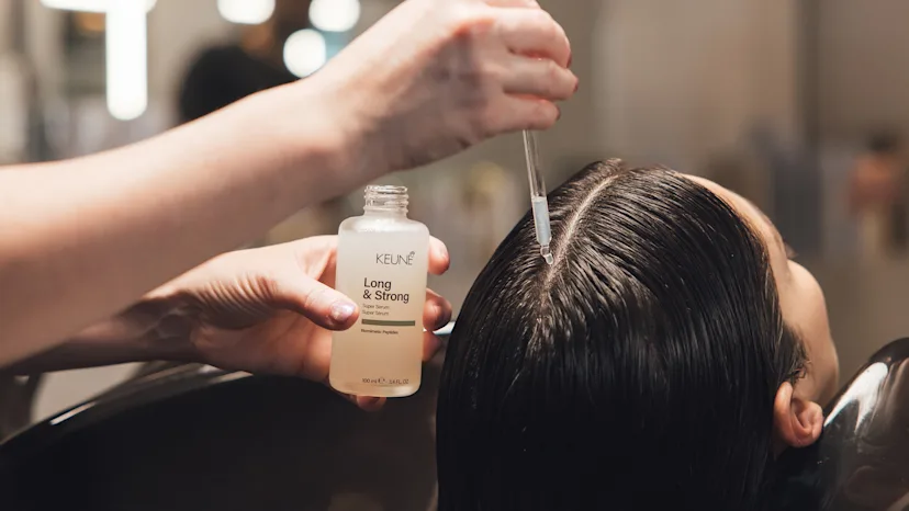 Een kapper die een serum aanbrengt op de hoofdhuid van een klant